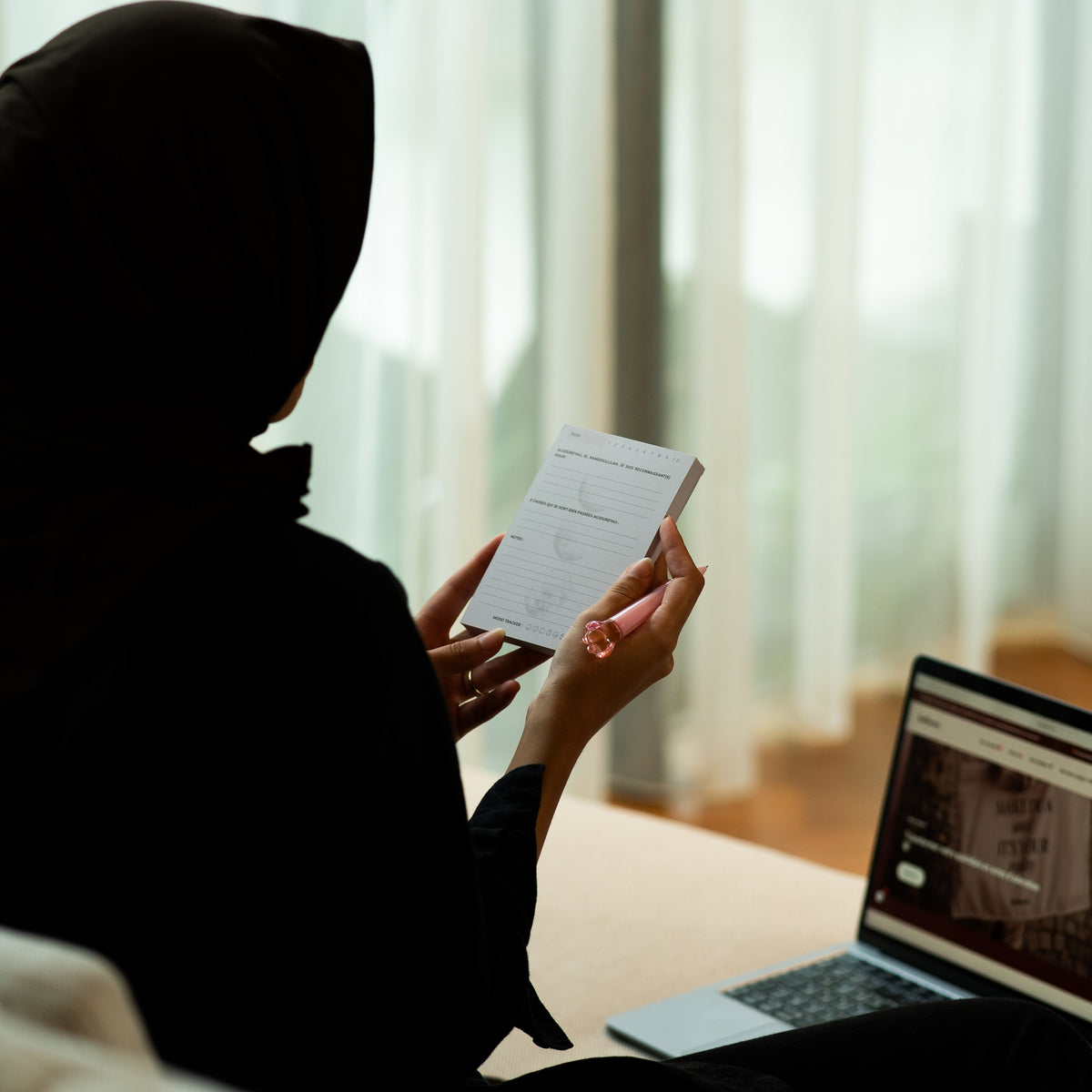 Une femme lit une carte Qalbeen, seule, près d'une fenêtre